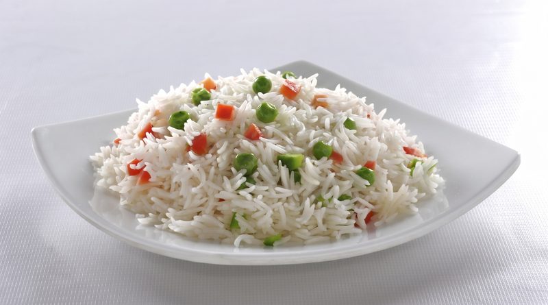 A serving of cooked white basmati rice with peas and diced vegetables on a white plate