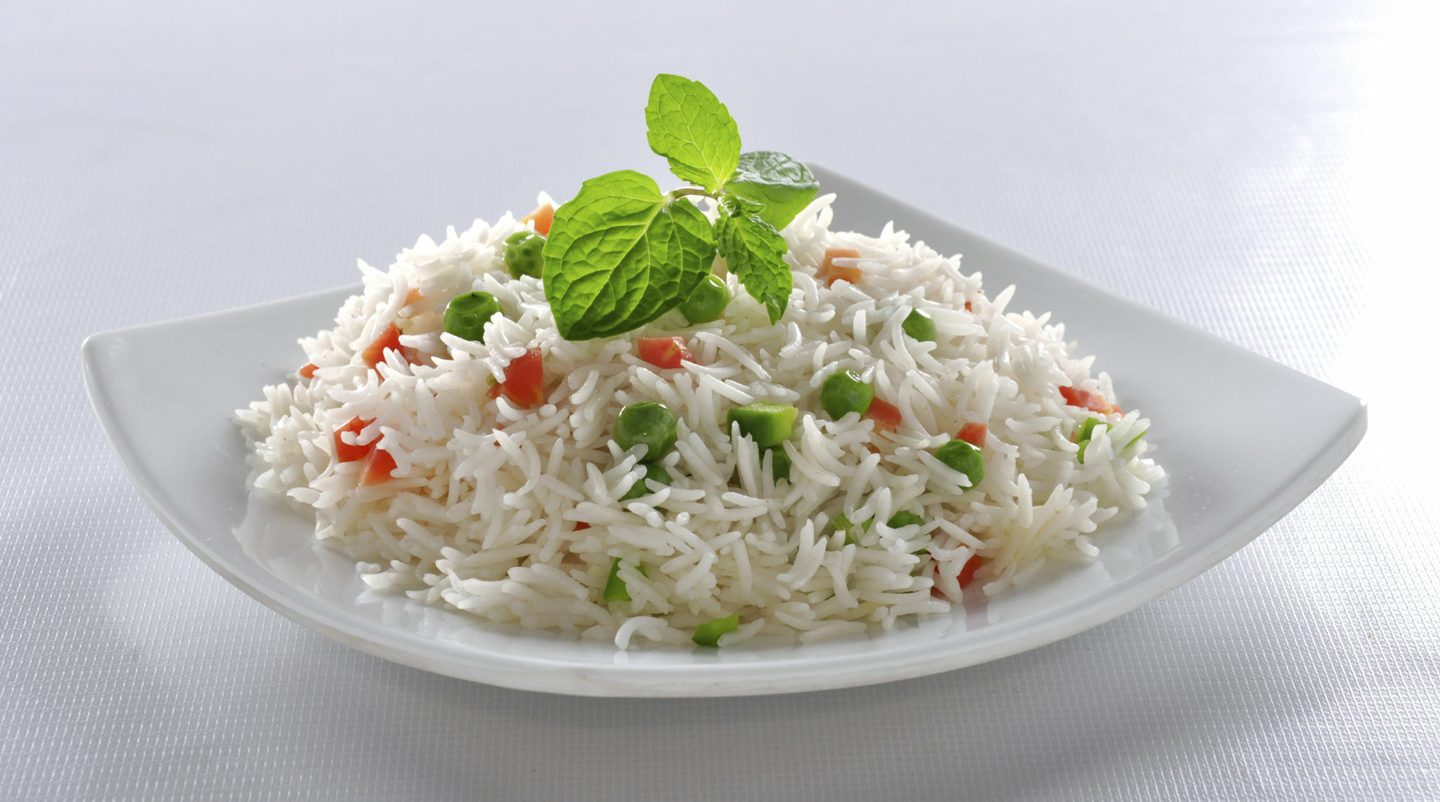 Cooked basmati rice garnished with fresh herbs on a white plate