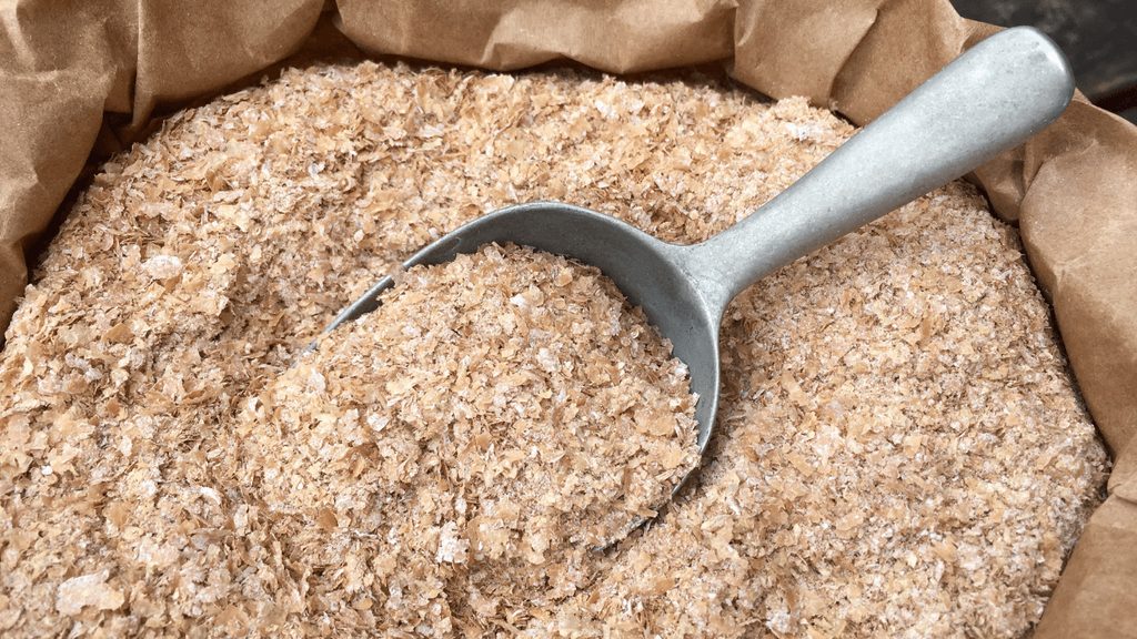 Golden wheat bran with a metal scoop resting in an open paper sack